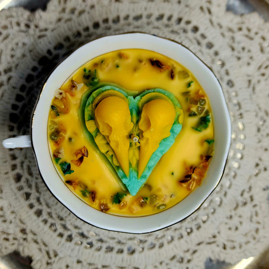 Yellow tea cup candle with green heart-shaped object on a textured surface